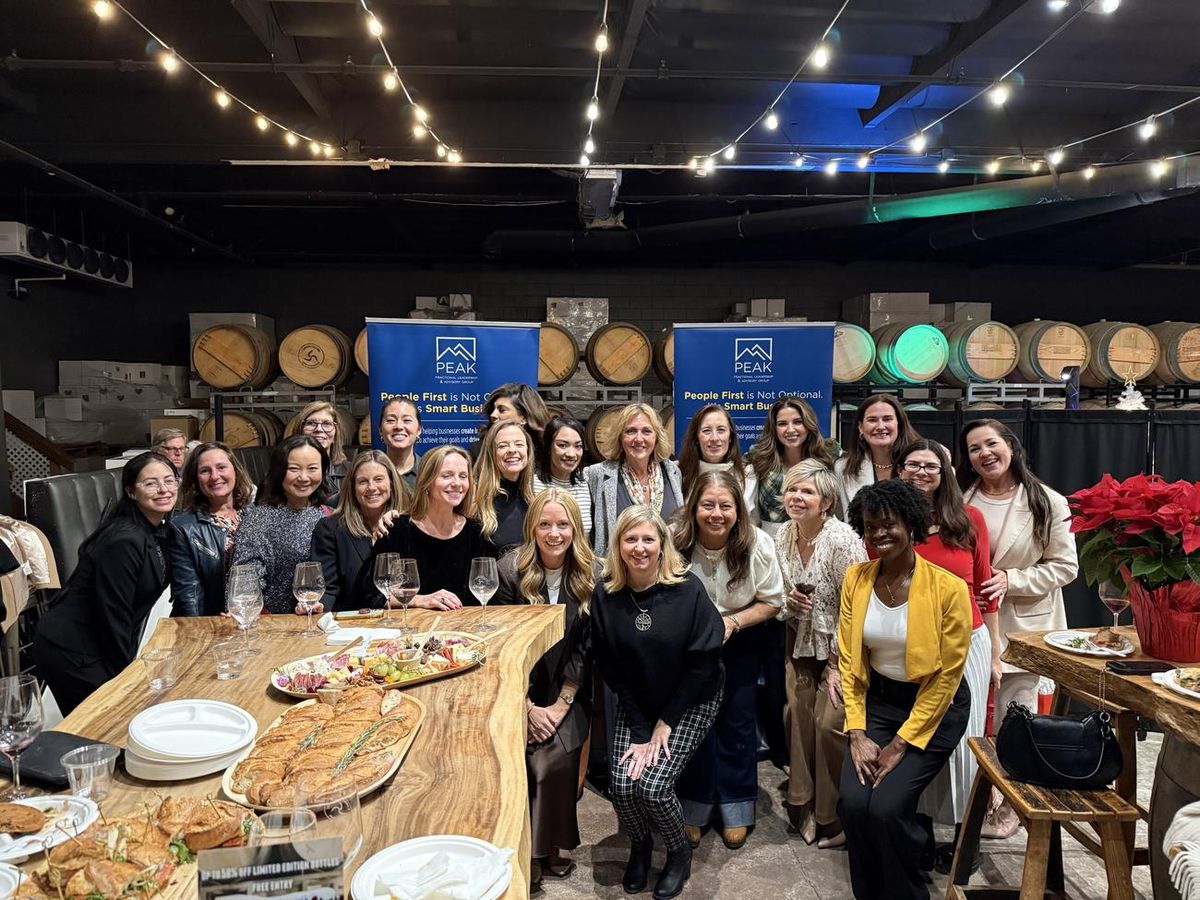 A room of Peak community members around a long table at a winery evening, with Peak banners behind them
